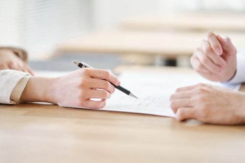 明るい木製テーブルで、ペンを持ち説明すつ住宅会社のスタッフ