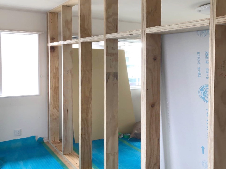 既存の床や家具をしっかりと養生し、大工が新しい間仕切り壁の枠組みを正確に施工。